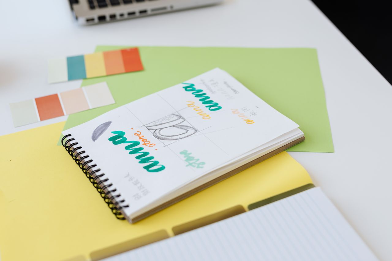 services-03 Gros plan sur des esquisses de design colorées dans un carnet à spirale, avec des nuanciers sur un bureau blanc.